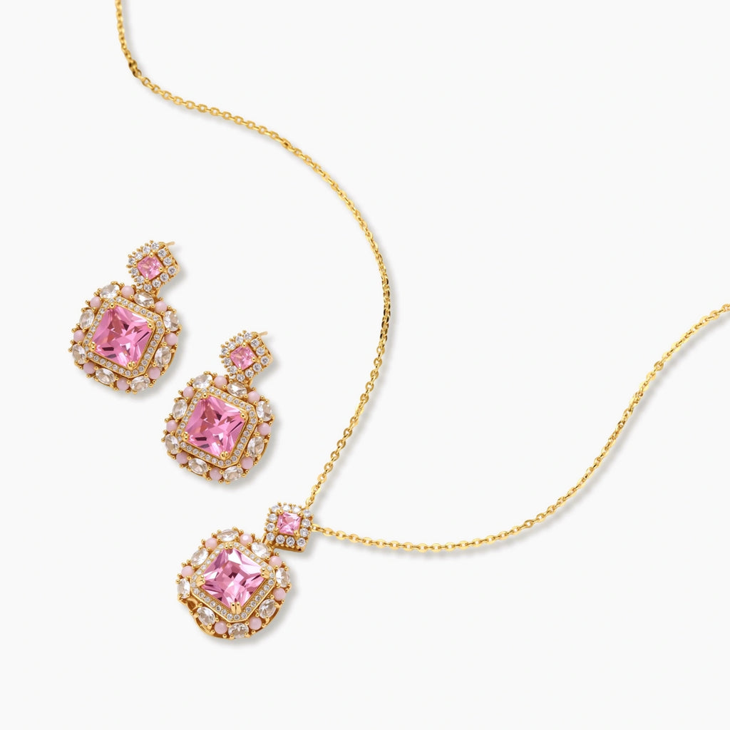 Ornate gold-plated jewelry set with rose pink zirconia center stones and crystal accents on cream background.