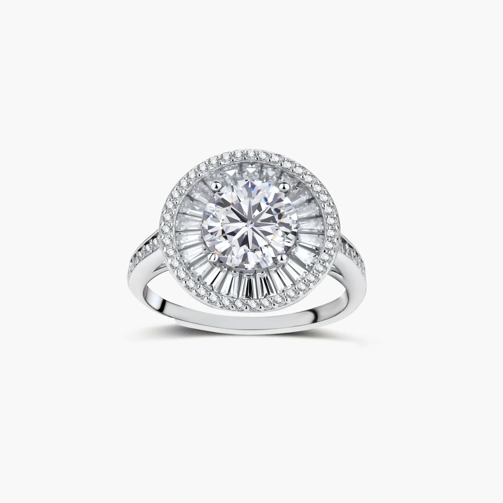 Brilliant round moissanite center stone with baguette and round halo accents in sterling silver setting on light background.
