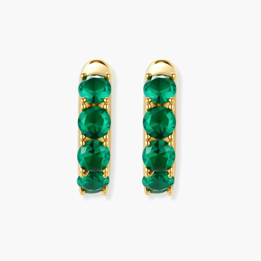 Close-up of gold-plated huggie hoop earrings featuring four emerald green cubic zirconia stones on white background.