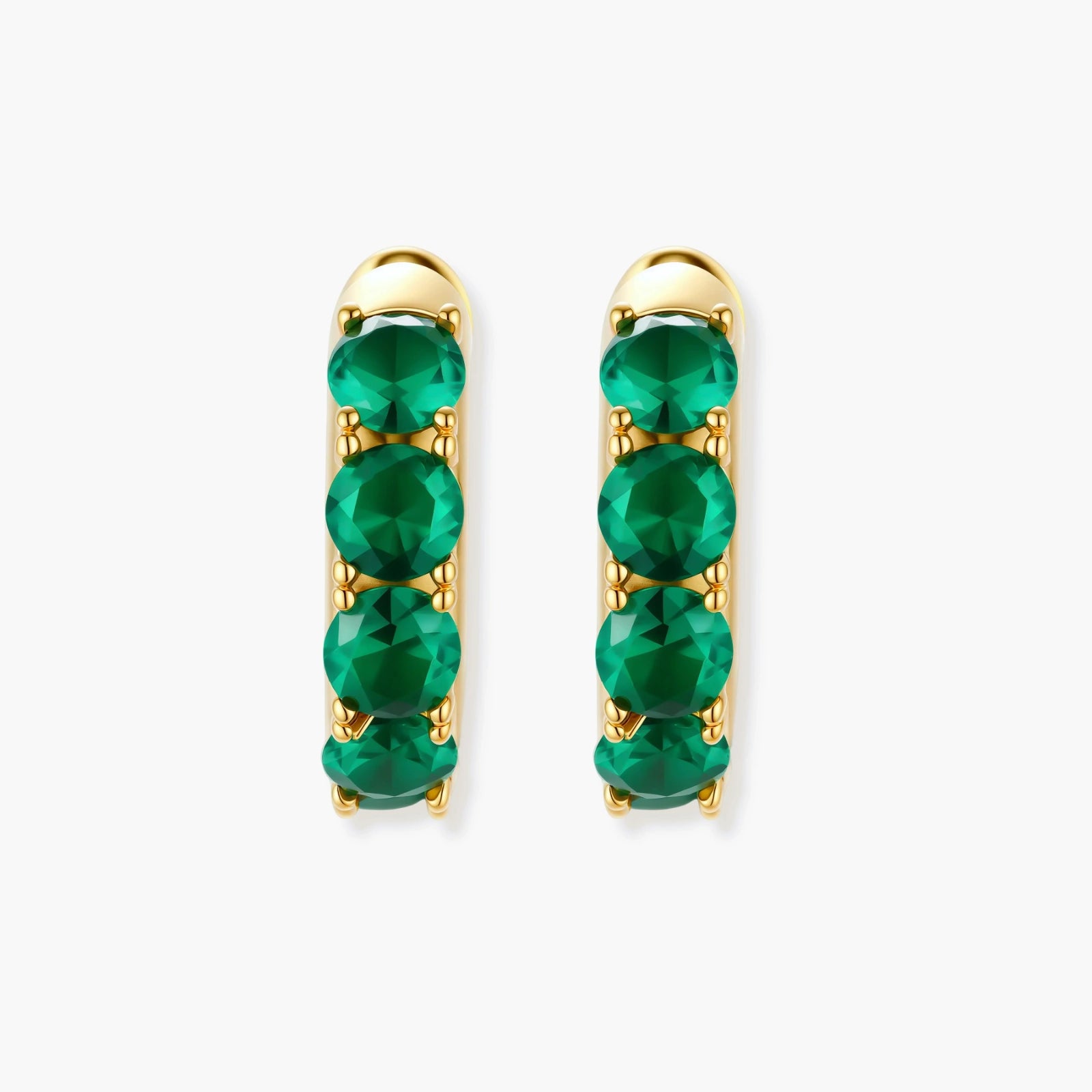 Close-up of gold-plated huggie hoop earrings featuring four emerald green cubic zirconia stones on white background.