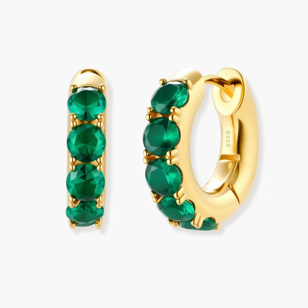 Close-up of gold-plated huggie hoop earrings featuring four emerald green cubic zirconia stones on white background.