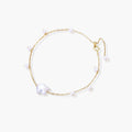 Delicate gold chain bracelet with baroque pearl centerpiece and small freshwater pearls on cream background.