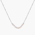 Delicate sterling silver chain necklace with small freshwater pearls arranged in a curved smile arc on cream background.