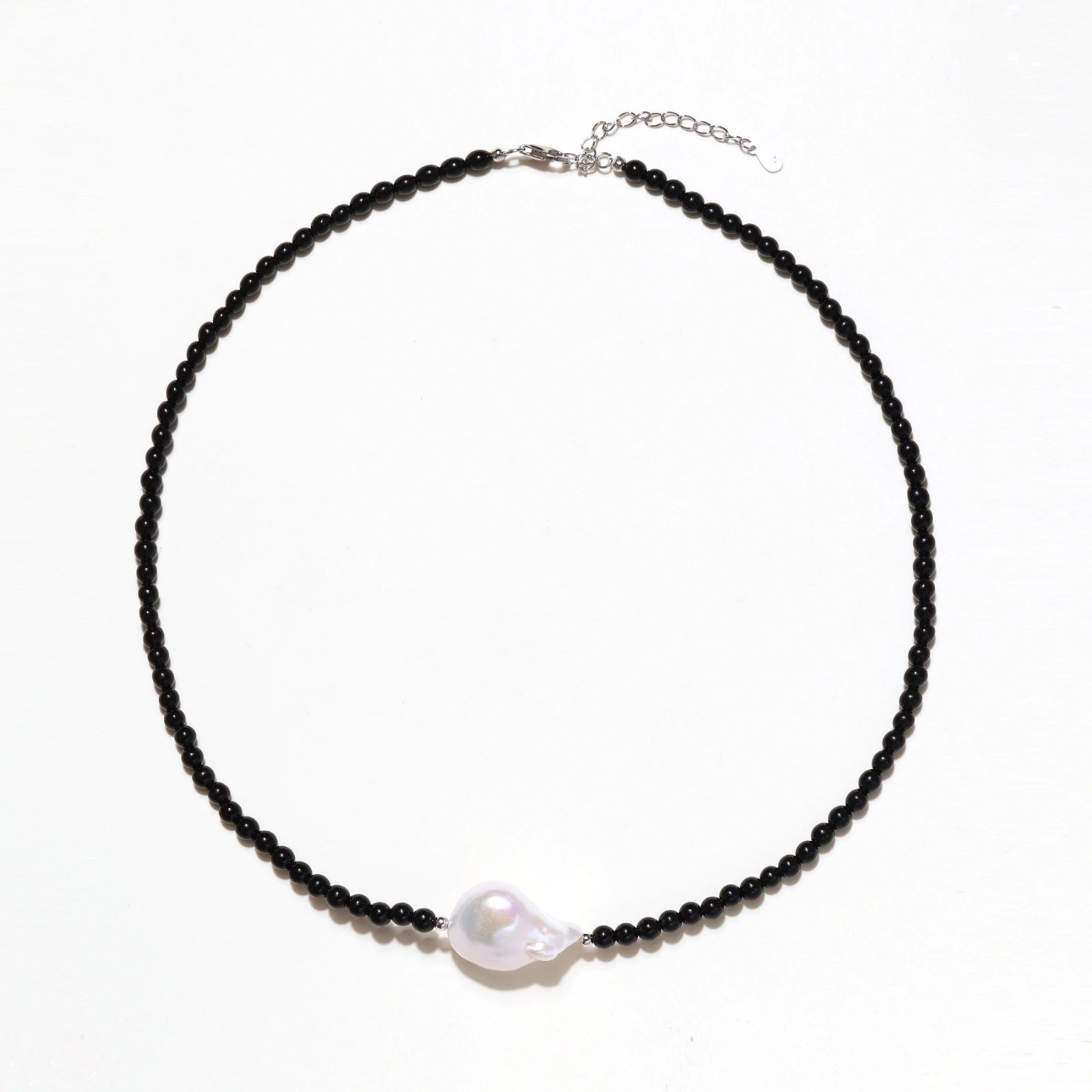 Beaded black agate necklace with iridescent baroque freshwater pearl centerpiece on cream background.