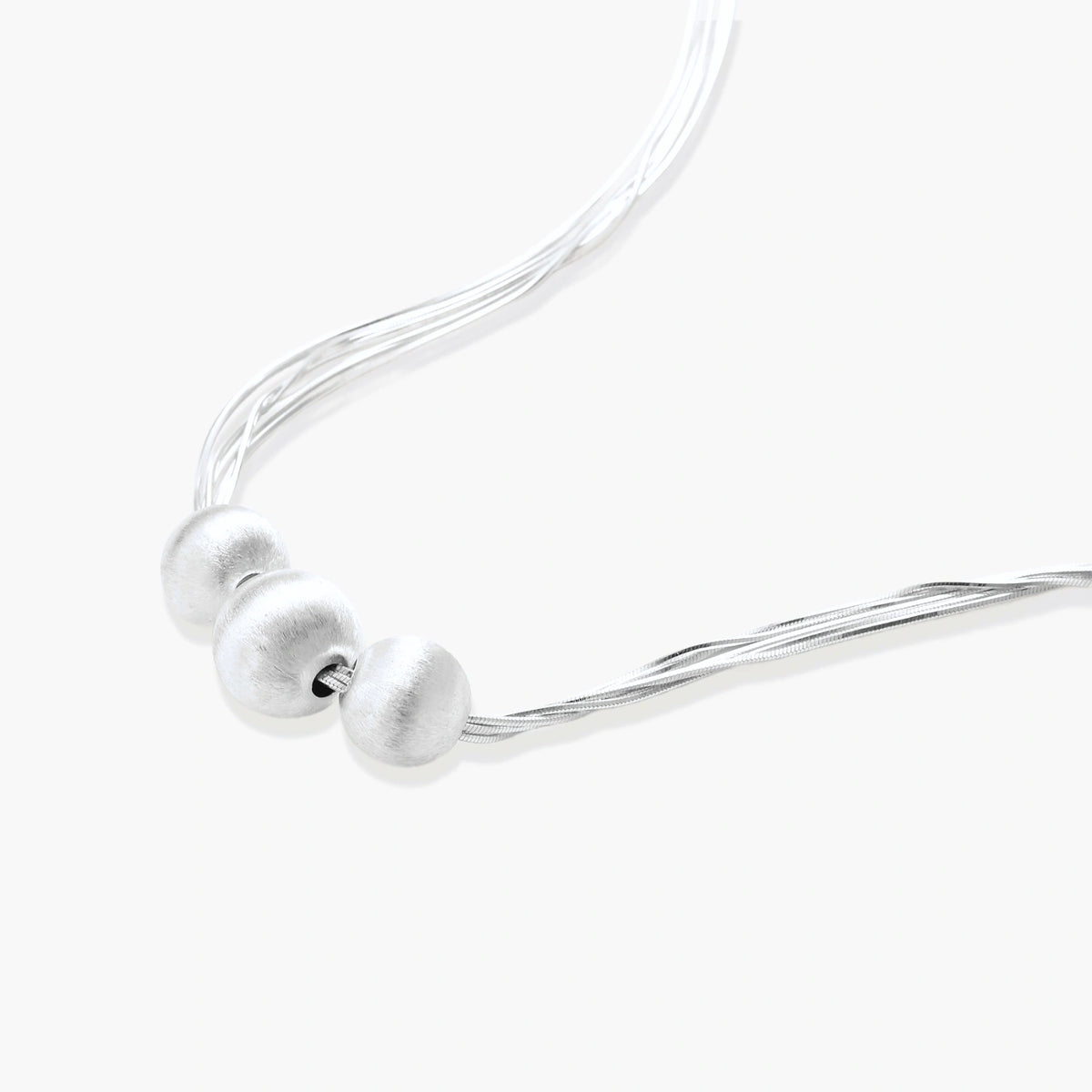 Sterling silver multi-strand necklace with three brushed round beads on cream background