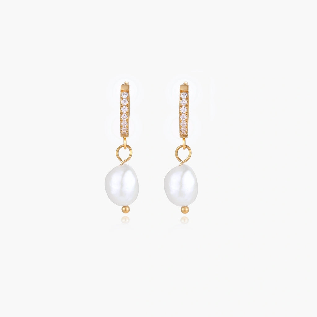 Gold huggie hoop earrings with pavé crystals and white freshwater pearl drops on cream background