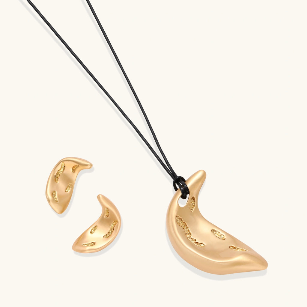 Gold-toned crescent moon pendant with textured surface on black adjustable cord, displayed with matching crescent earrings