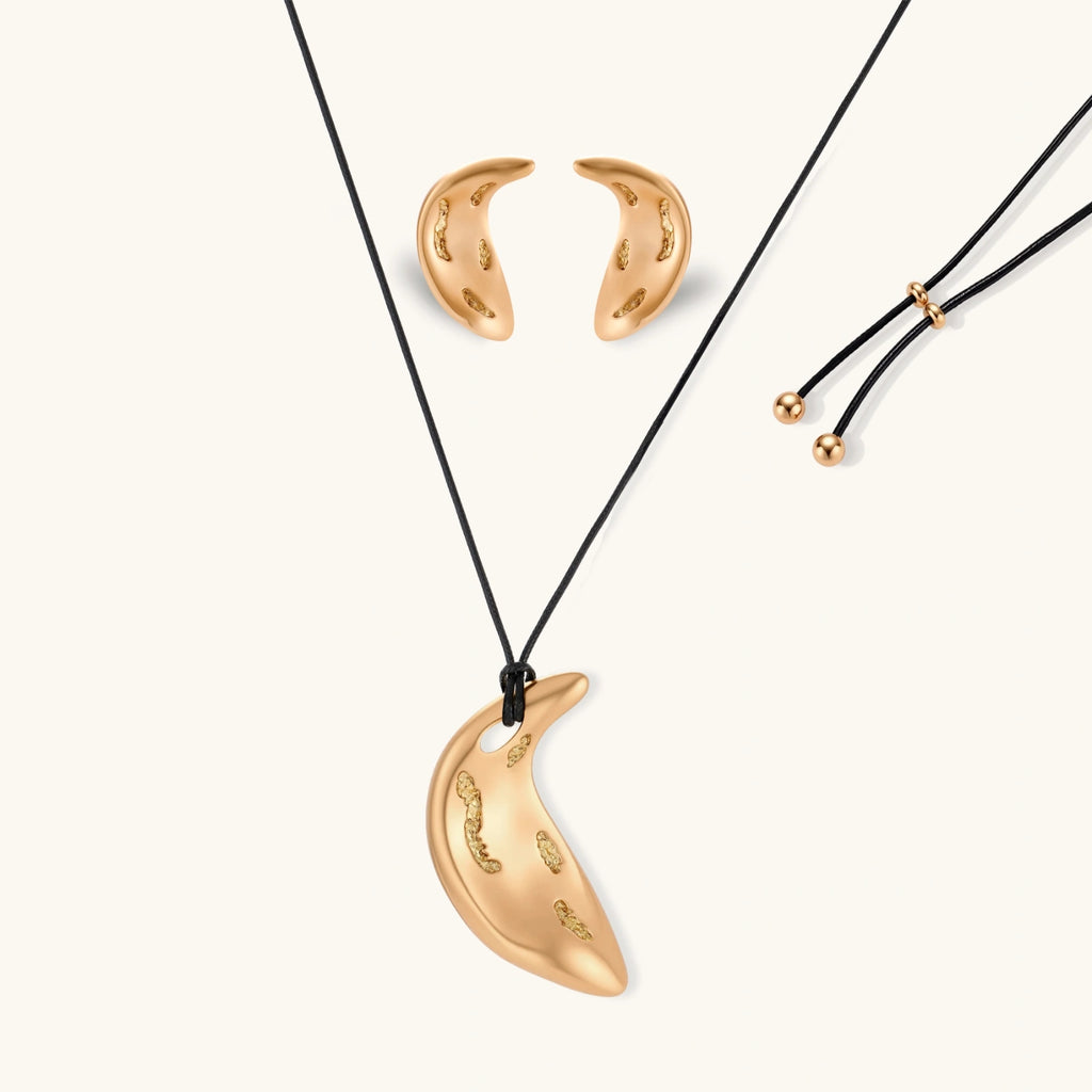 Gold-toned crescent moon pendant with textured surface on black adjustable cord, displayed with matching crescent earrings