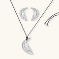 Crescent moon shaped pendant and earrings in eco-zinc alloy with curved crystal inlay patterns on light background.