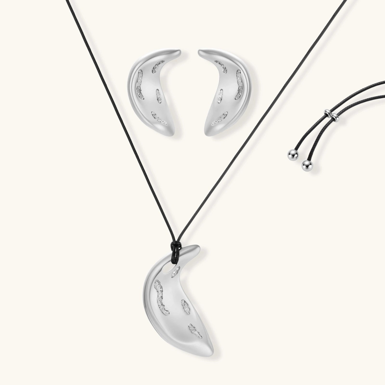 Crescent moon shaped pendant and earrings in eco-zinc alloy with curved crystal inlay patterns on light background.