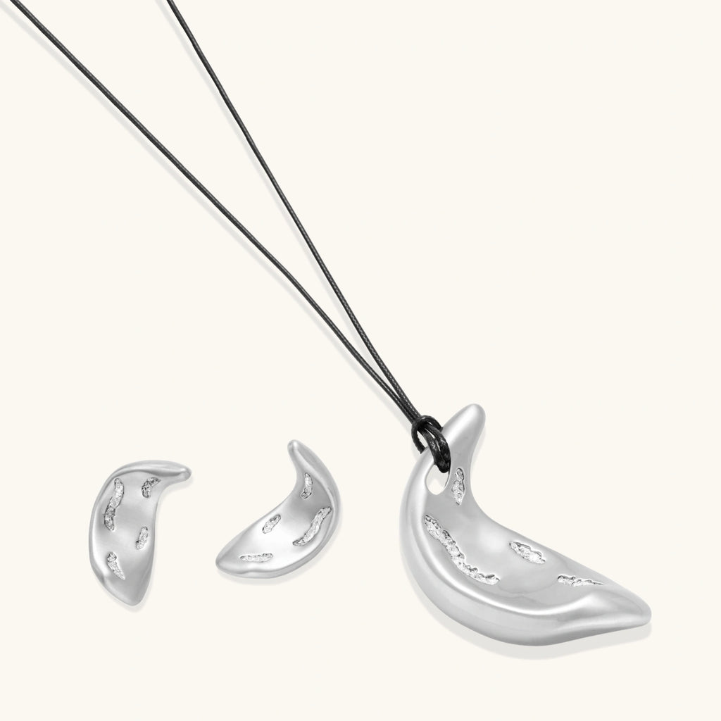 Crescent moon shaped pendant and earrings in eco-zinc alloy with curved crystal inlay patterns on light background.