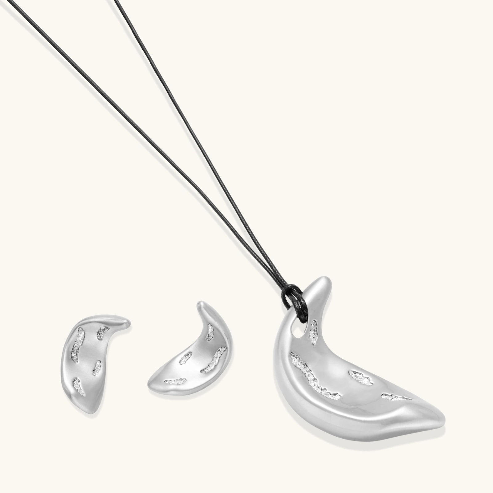 Crescent moon shaped pendant and earrings in eco-zinc alloy with curved crystal inlay patterns on light background.