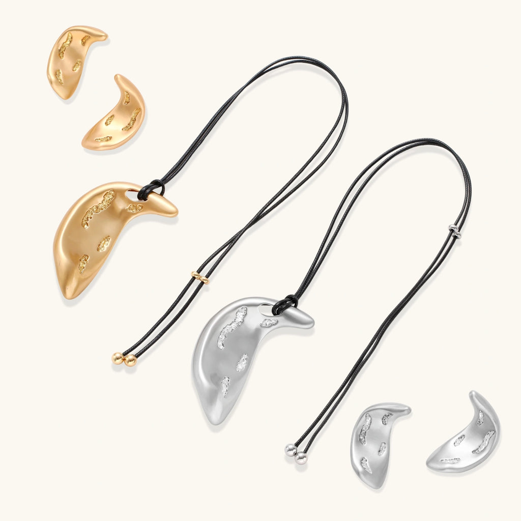 Crescent moon shaped pendant and earrings in eco-zinc alloy with curved crystal inlay patterns on light background.