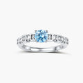 Geometric sterling silver ring with light blue moissanite center stone and square diamond accents on white background