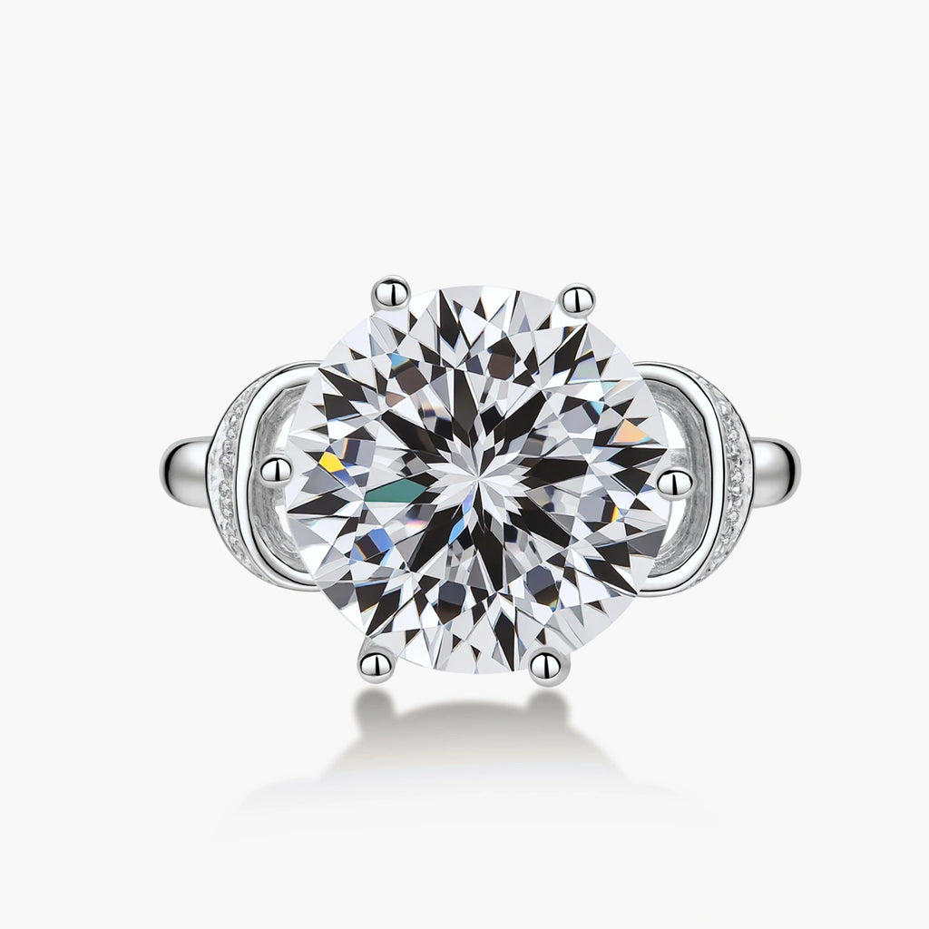 Sterling silver ring with 5ct round moissanite center stone and intricate bow design with pavé accents on white background.