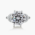Sterling silver ring with 5ct round moissanite center stone and intricate bow design with pavé accents on white background.