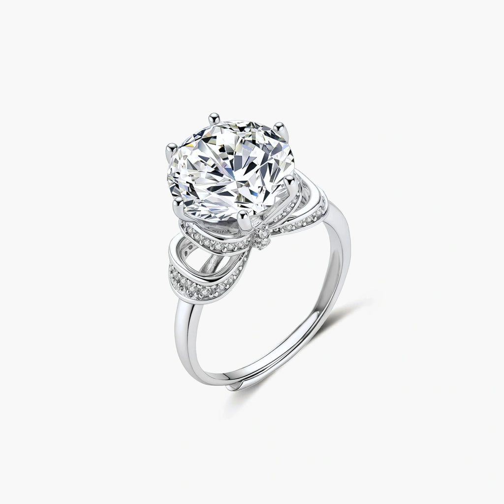 Sterling silver ring with 5ct round moissanite center stone and intricate bow design with pavé accents on white background.