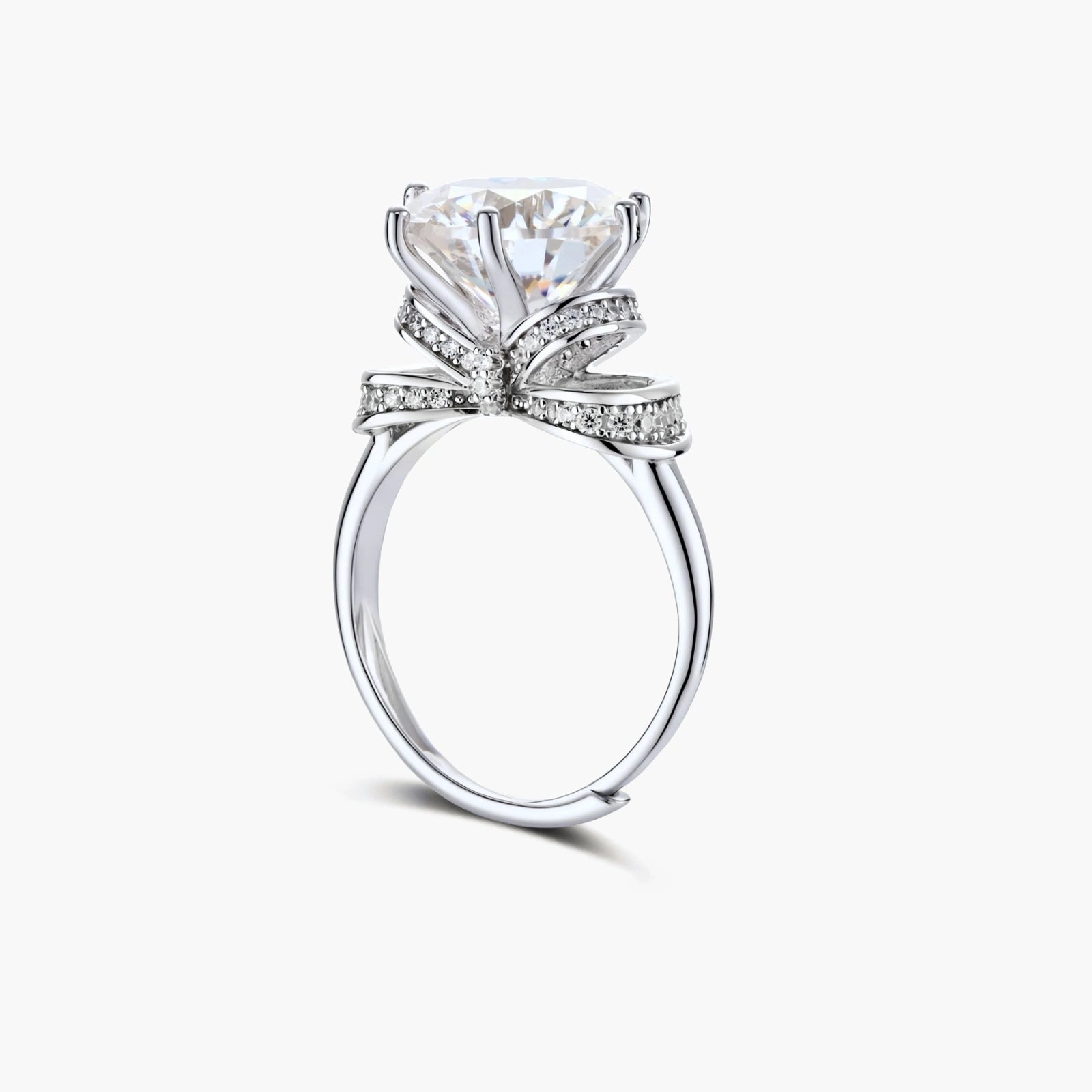 Sterling silver ring with 5ct round moissanite center stone and intricate bow design with pavé accents on white background.