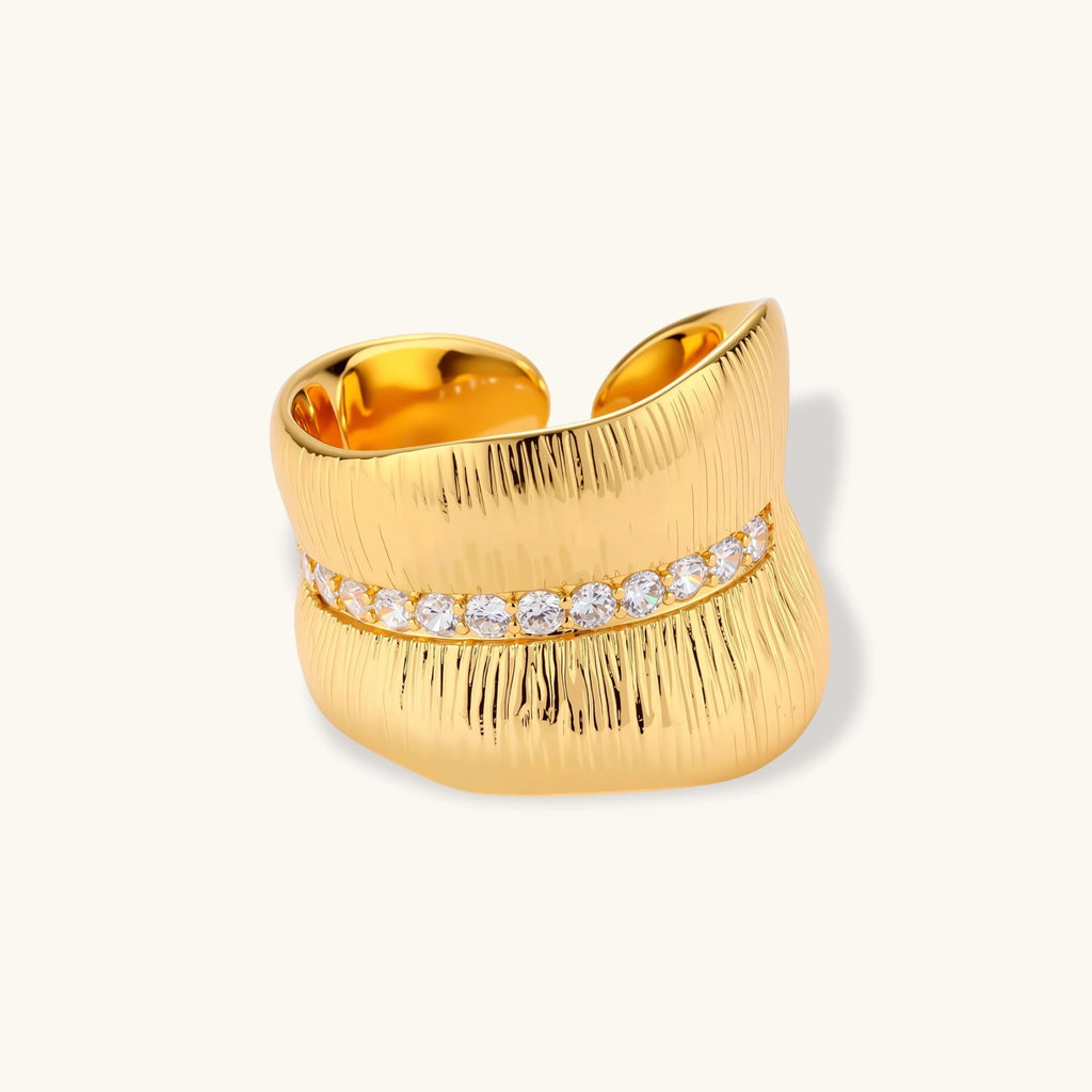 Adjustable gold-plated cuff ring with parallel ridged texture and diagonal row of sparkling zirconia stones on white background.