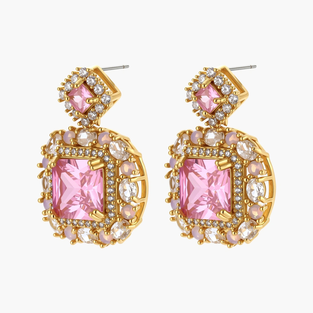 Ornate gold-plated jewelry set with rose pink zirconia center stones and crystal accents on cream background.