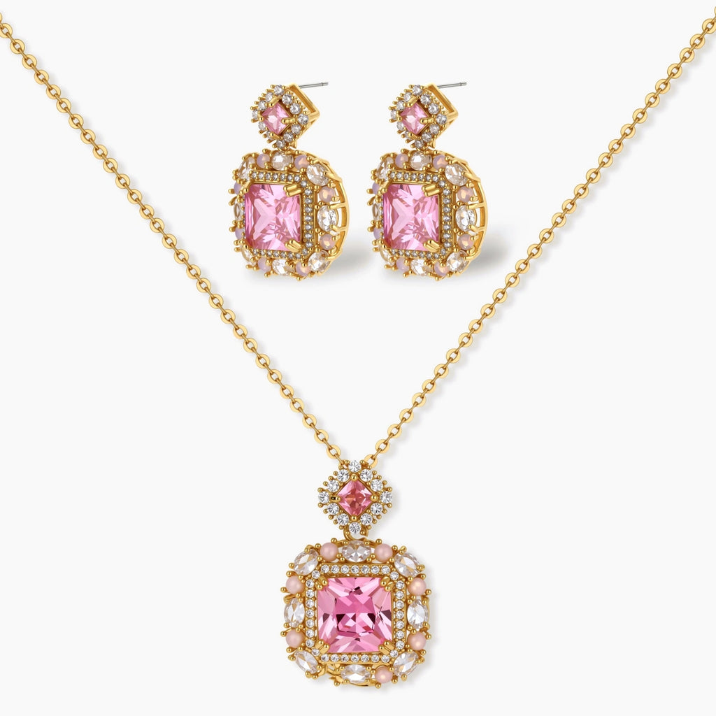 Ornate gold-plated jewelry set with rose pink zirconia center stones and crystal accents on cream background.