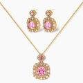 Ornate gold-plated jewelry set with rose pink zirconia center stones and crystal accents on cream background.