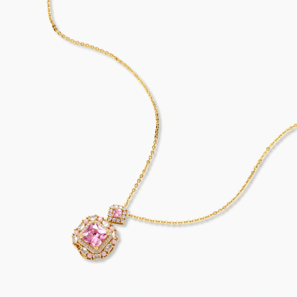 Ornate gold-plated jewelry set with rose pink zirconia center stones and crystal accents on cream background.